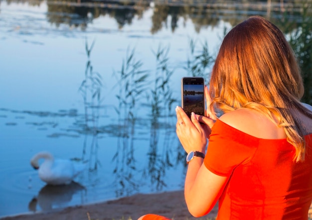 Girl on the shore of a lake taking a picture of a swan