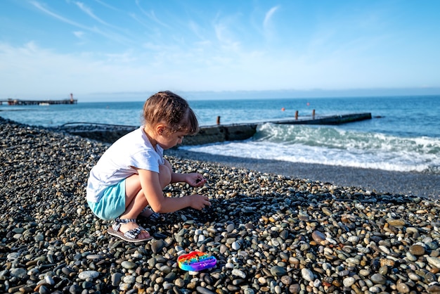 A girl in shorts and a T-shirt plays stones on the seashore and pops it on an early summer morning.