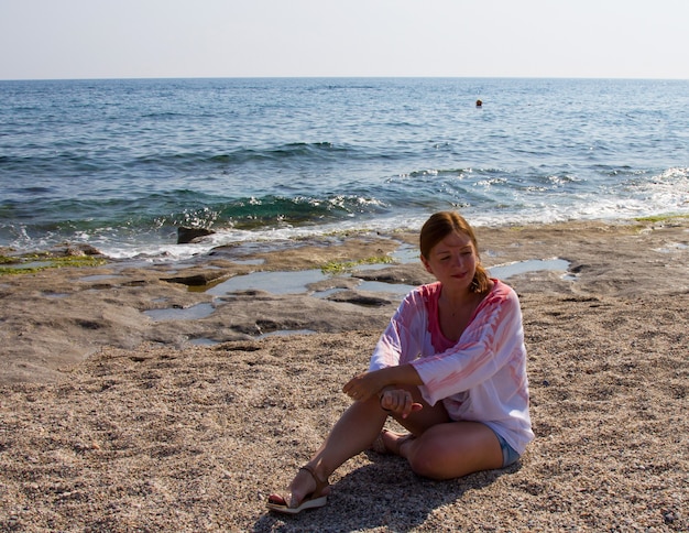 Photo girl in shorts and white blouse on the beach by the sea.. red-haired woman on a sandy beach. a holiday in the south