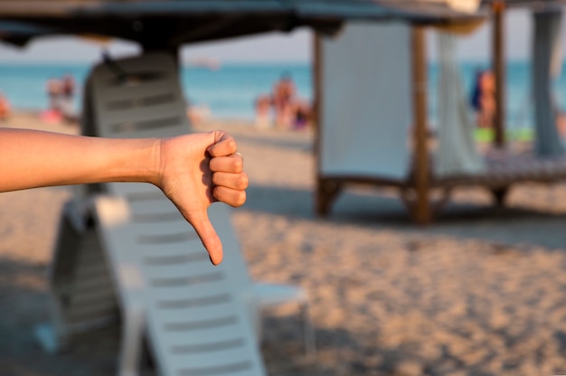 Girl showing her disliking to sea, beach with her thumb down