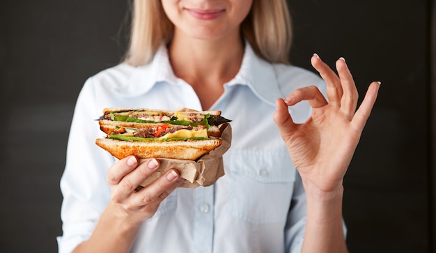 Girl showing ok holding a sandwich