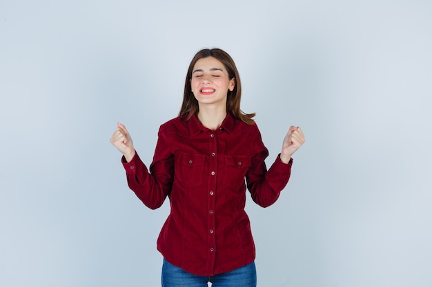 Girl showing winner gesture in burgundy blouse and looking victorious.