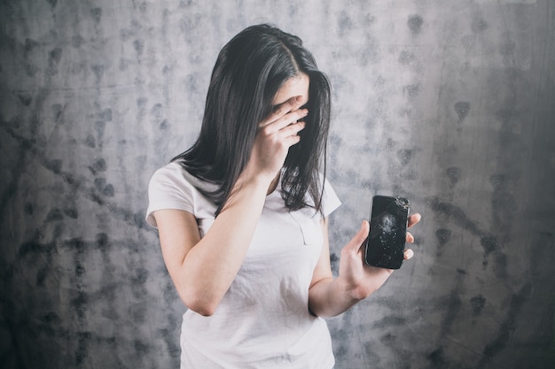 La ragazza mostra un telefono rotto.