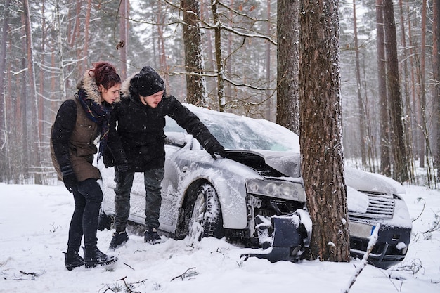 Photo girl shows her boyfriend the damage to his car after the accident. the girl crashed her boyfriend's car. crashed car after accident in snowy forest