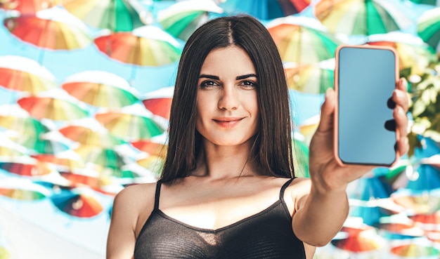 Girl shows a phone screen on a background of colorful umbrellas Portraite