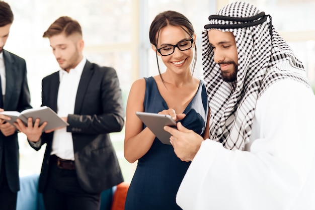 Una ragazza mostra qualcosa a un uomo in abiti arabi su tablet.