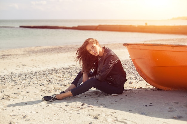 A girl sideways near a red boat on the beach by the sea