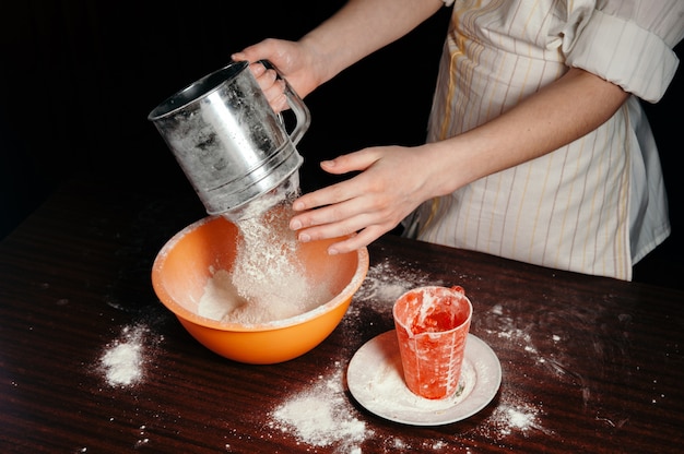 The girl sifts the flour in a steel sieve. 