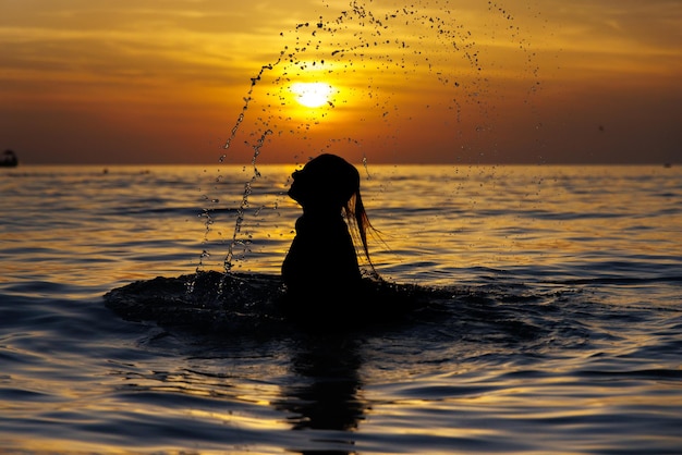 Photo the girl silhouette emerged from the sea with splashes at sunset