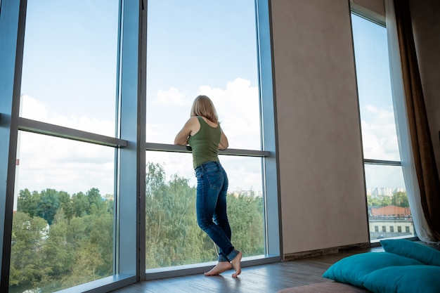 街の建物の外に大きな窓からすの近くの女の子のシルエットが見えます。夢。心のトラブル。 Problems.panoramic Windows.Back view.Copy space