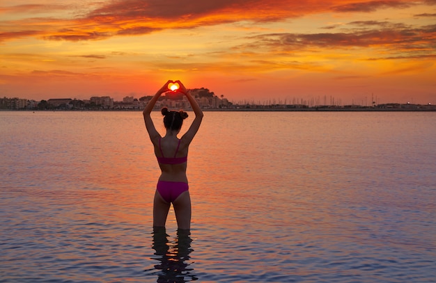 Girl silhouette at sunset heart shape hands