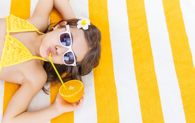 Photo girl sipping juice from orange fruit through straw lying on towel