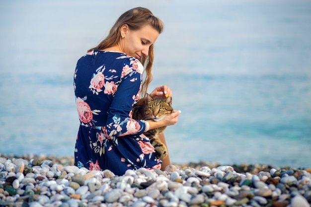 The girl sits a back on the bank of the Mediterranean Sea and irons a cat