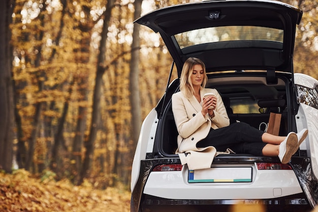 La ragazza si siede sul retro dell'auto. automobile nuova di zecca moderna nella foresta.