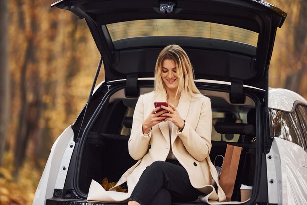 Girl sits on the back of car. modern brand new automobile in the forest.