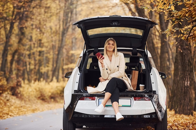 Girl sits on the back of car. Modern brand new automobile in the forest.