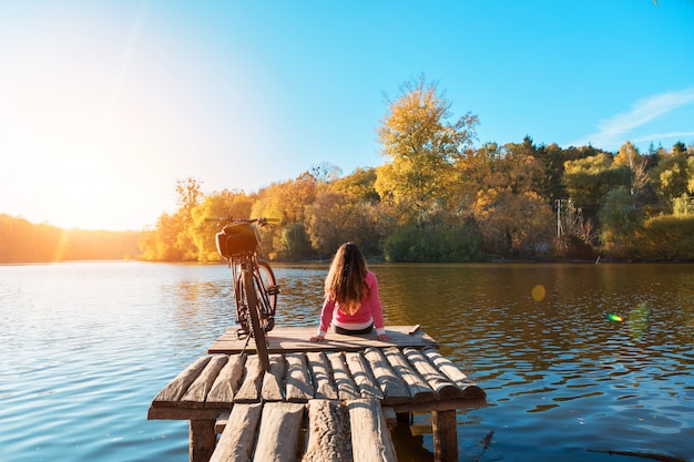 Girl sits on the bank of the river. bike on the river with a bag on the trunk