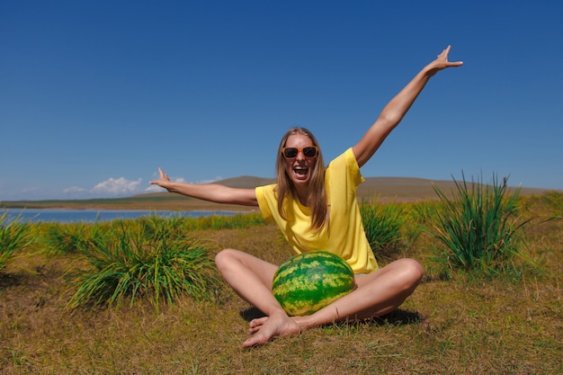 A girl sits on the beach and holds a watermelon. ripening of summer berries Joyful emotions and mood. Summer picnic.