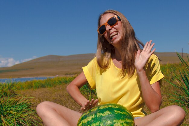 A girl sits on the beach and holds a watermelon ripening of summer berries joyful emotions and mood ...