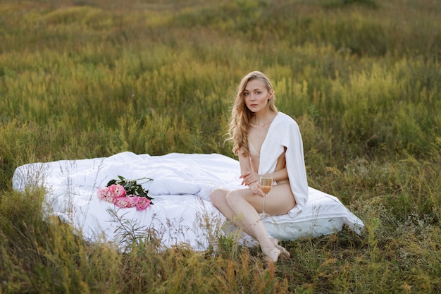 A girl sits on a bed at sunset in the garden. next to her is a bouquet of peonies