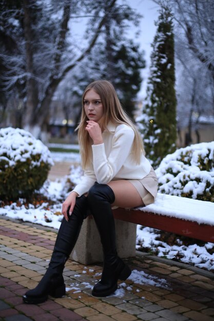 a girl sits on a bench in front of a snow covered tree