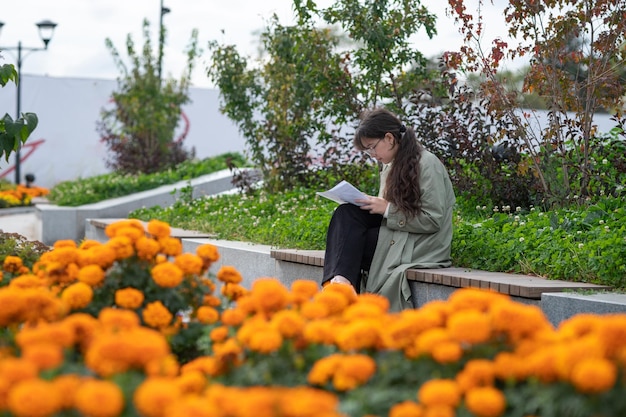 A girl sits on a bench on the street with documents in her hands and using her phone