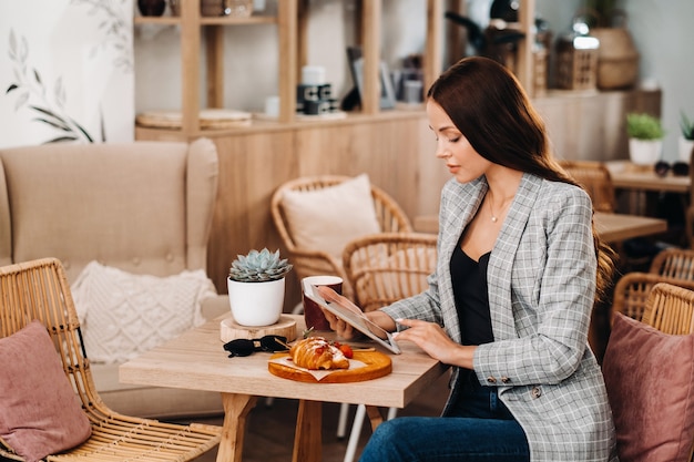 カフェに座ってタブレットを見る女の子、喫茶店の女の子が微笑む、遠い仕事。