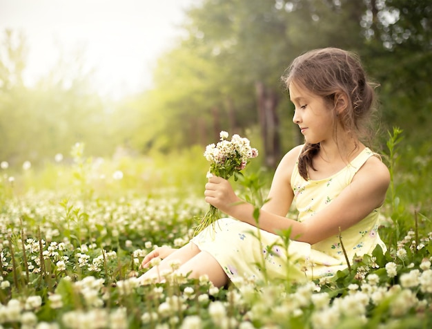 girl sits in a clearing of clover and collects a bouquet of flowers