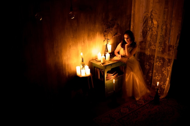 The girl sits in the corner of the room and reads by candlelight. Candle light, top view