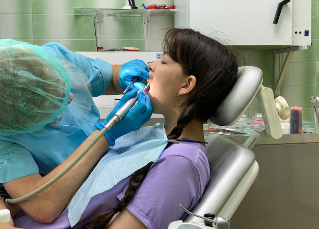 A girl sits in a dentist's chair, which she conducts an ultrasonic cleaning of her teeth.