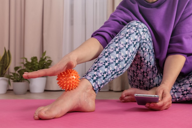 Girl sits on floor and massages herself with prickly ball to\
relax and circulate