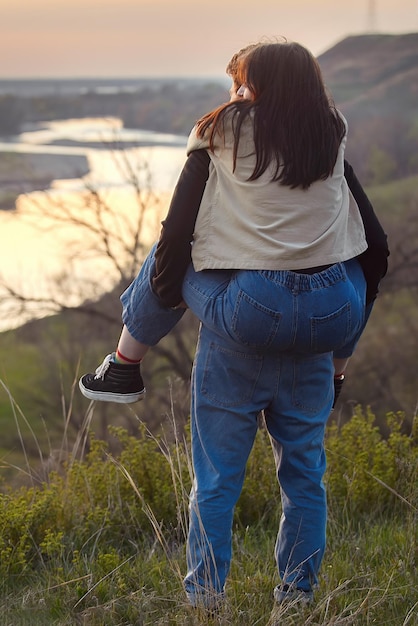 한 소녀는 남자 친구의 등에 앉아 자연의 일몰을 감상한다