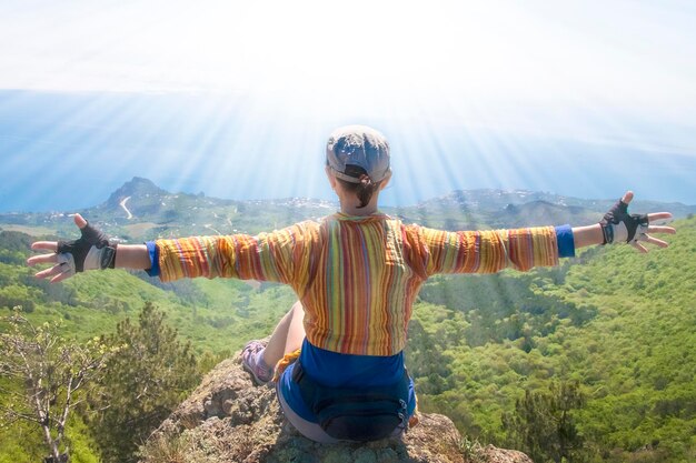 The girl sits on a high mountain hands wide apart