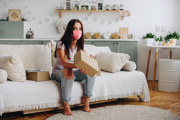 Photo the girl sits at home on a sofa in a mask holds a box in her hands received delivery