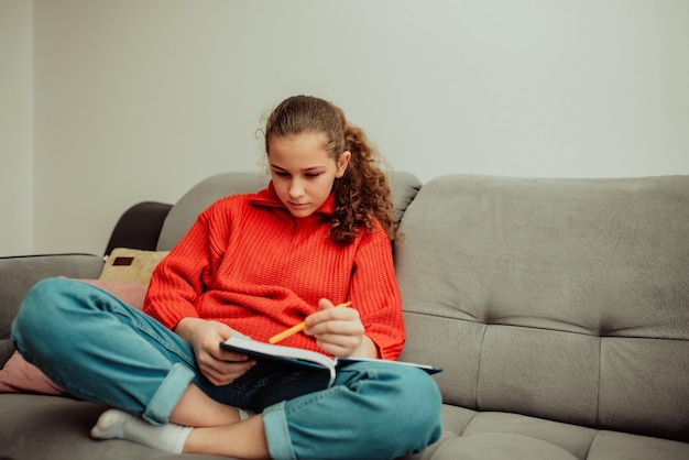 The girl sits in the house and writes homework in a notebook