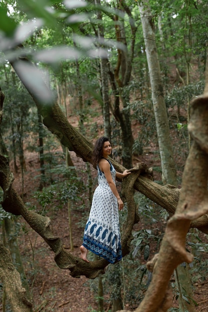 The girl sits on a huge liana tree branch in the jungle.