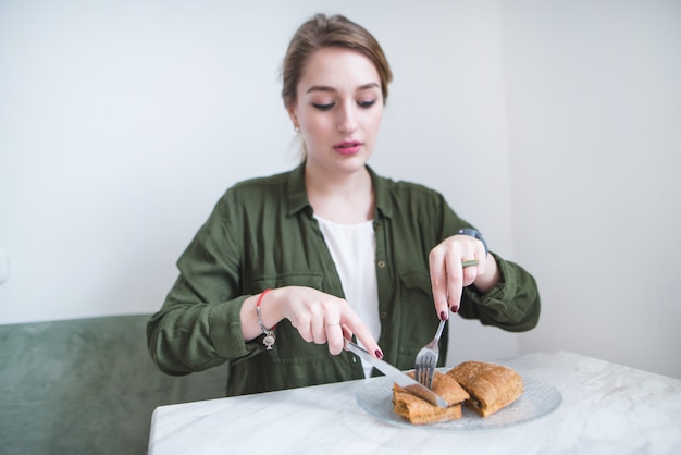 Photo girl sits in light restaurant and eats sandwich with knife and fork. woman is having breakfast at cafe.