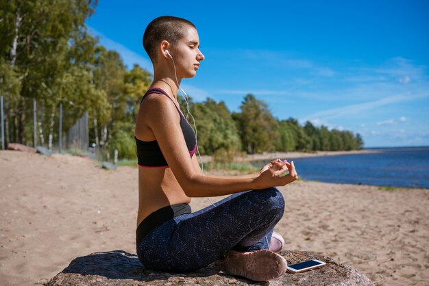 Girl sits in lotus position on beach and meditates on sunny day listening