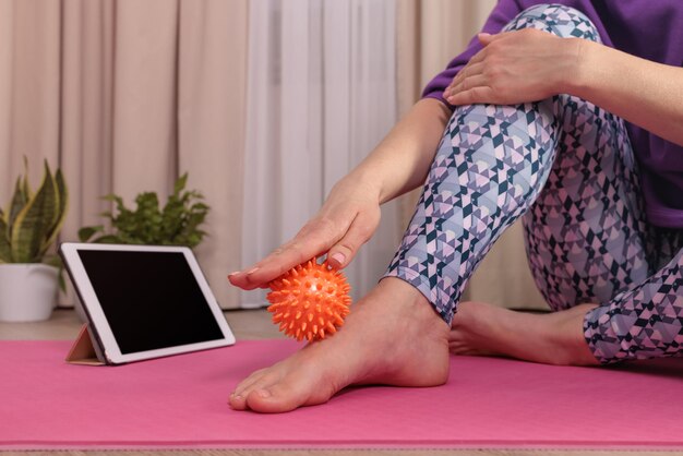 the girl sits and massages herself with a ball to relax looks at the tablet