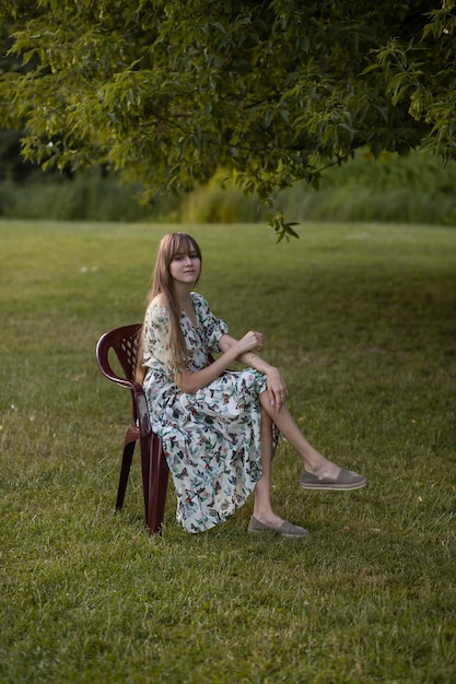 a girl sits in a park on an armchair in a vintage flowered dress. Retro dress and vintage atmospheri