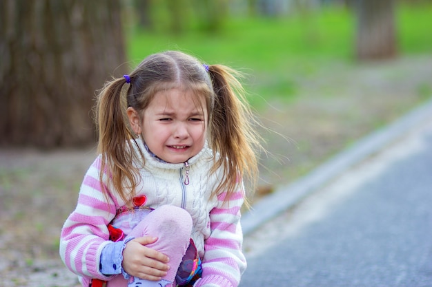 The girl sits on the road and cries, holding a knee