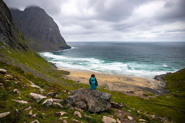 소녀는 노르웨이 로포텐 섬의 크발비카 해변 꼭대기에서 전망을 즐기는 바위 위에 앉아 있다