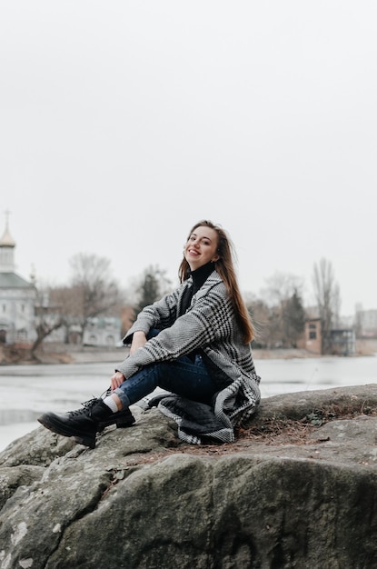 A girl sits on a rock in front of a river