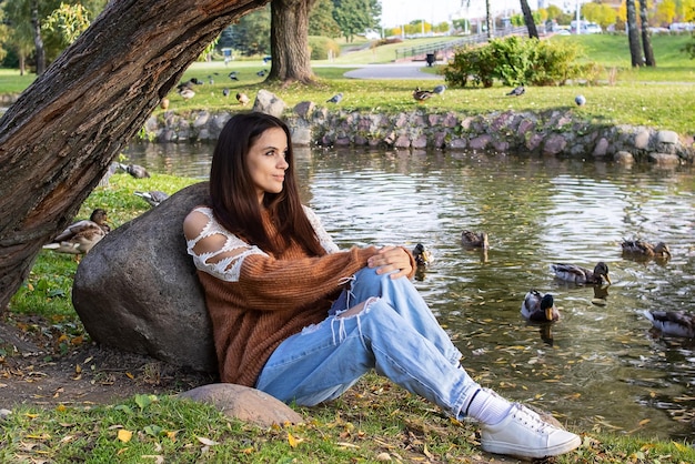 A girl sits on the shore of a pond