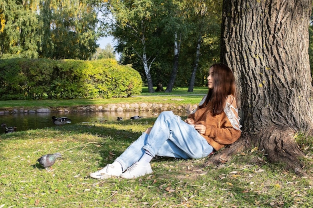 A girl sits on the shore of a pond