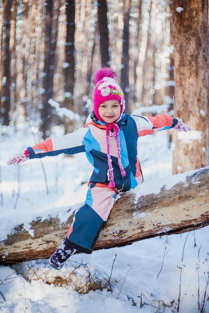 女の子は森のオーバーオールで雪の上に座っています