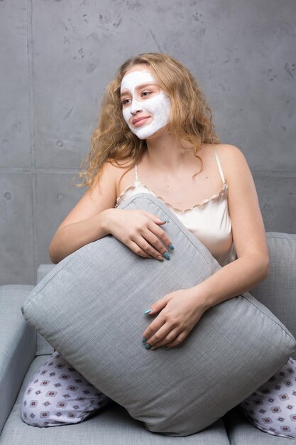 La ragazza si siede sul divano con indosso una maschera cosmetica