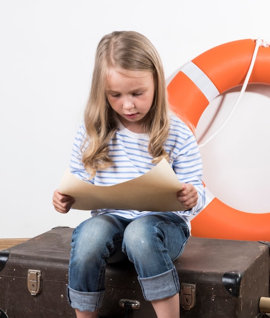 A girl sits on a suitcase and reads a list Girl playing on a trip