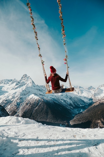 Photo the girl sits on a swing in the mountains from the back. heavenly swing over the abyss.