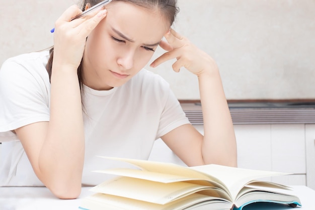 A girl sits at a table and thinks next to a book